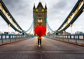 A view of a person holding a red heart shaped umbrella standing on the main road on Tower Bridge